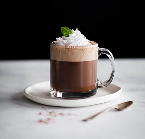 Peppermint Mocha Coffee drink in a glass mug with foam and whipped cream garnished with a mint leaf