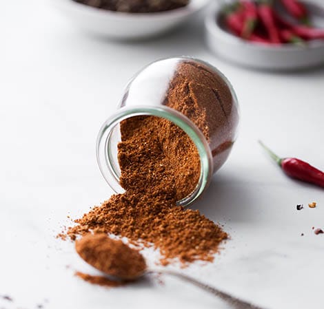 Taco Seasoning Ground taco seasoning in a glass container with chiles in the background