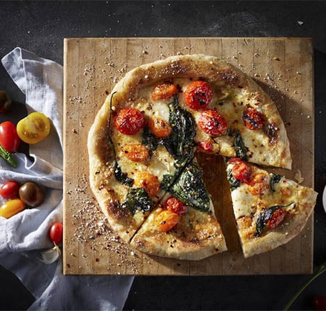 Pizza pizza with basil and tomatoes on it on a cutting board